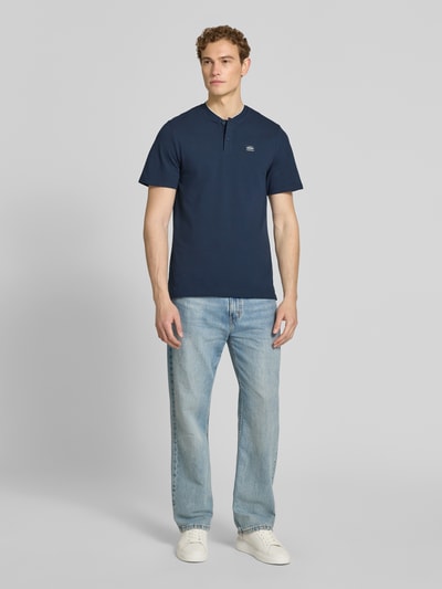 Männermodel trägt Regular Fit Poloshirt aus Baumwoll-Mix von s.Oliver RED LABEL, unifarben, kurzarm, 2-Knopf-Henley Ausschnitt, Ganzkörperansicht von vorne.