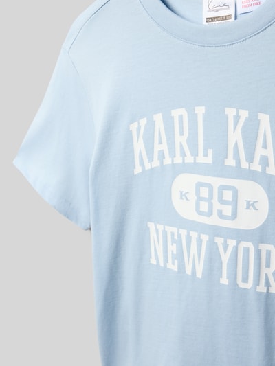 Mädchen trägt Regular Fit T-Shirt mit Logo-Print von KARL KANI aus Reine Baumwolle in Hellblau, Rundhalsausschnitt, Nahaufnahme Oberkörper.