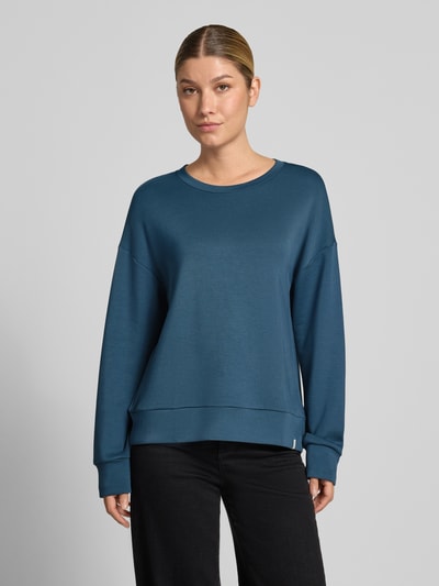 Modelka nosi bluzę 'Sweatshirt mit Rundhalsausschnitt und Label-Detail' od SCHIESSER, mieszanka modalu z dodatkiem streczu, krój loose fit, okrągły dekolt, obniżone ramiona, detal z logo, kolor ciemnoniebieski, gładka struktura, widok całej sylwetki z przodu.
