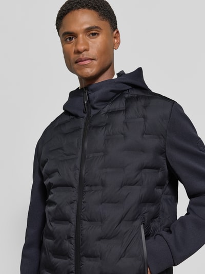 Männermodel trägt Regular Fit Steppjacke mit winddichter Funktion von Strellson in Dunkelblau, glatte Textur, Nahaufnahme Oberkörper, Herren Steppjacke von Strellson.