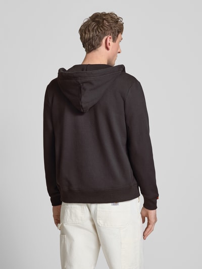 Männermodel trägt Sweatjacke mit Kapuze und Logo-Stitching von Superdry in Schwarz aus Baumwoll-Mix mit Gerippte-Abschlüsse, Rückenlänge 66 cm, Ganzkörperansicht Rückansicht.