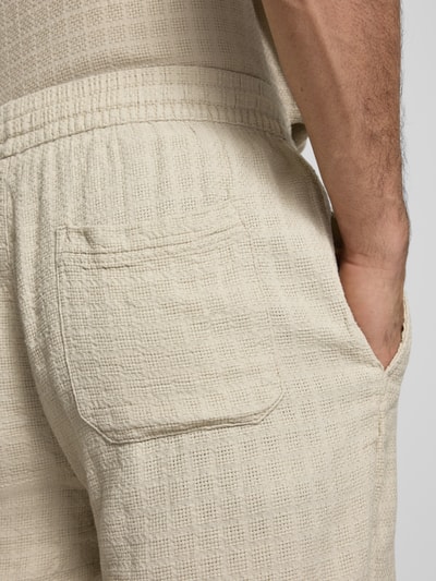 Männermodel trägt Regular Fit Shorts aus Viskose-Leinen-Mix Modell 'TEL LATHAM' von Only & Sons in Beige mit strukturierter Flammgarn-Optik, Tunnelzugbund und seitlicher Eingrifftasche, Nahaufnahme Rückansicht.