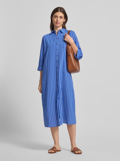 Kobiece modelka nosi Hemdblusenkleid aus Viskose-Mix mit Brusttasche od Milano Italy, sukienka midi, prosty krój, kołnierzyk koszulowy, brustasza, listwa guzikowa, rękaw o dł. 3/4, długość tyłu w rozmiarze 36: 118 cm, szerokość w rozmiarze 36: 53 cm, długość rękawów w rozmiarze 36: 43 cm, niebieskie pionowe paski, gładka faktura, pełny widok z przodu.