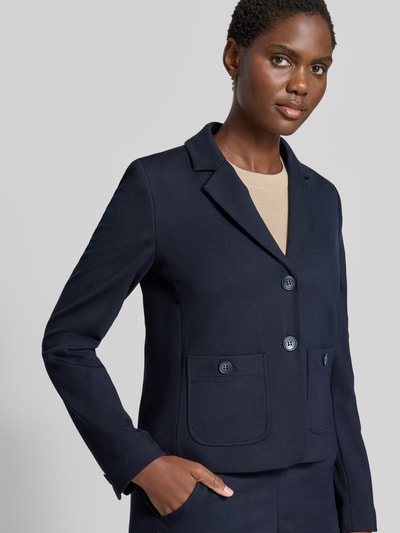 Frauenmodel trägt Blazer aus Viskose-Mix mit Reverskragen von MORE & MORE in Dunkelblau, tailliert, Nahaufnahme Oberkörper. Elastischer Stoff, aufgesetzte Taschen, 2-Knopfleiste.
