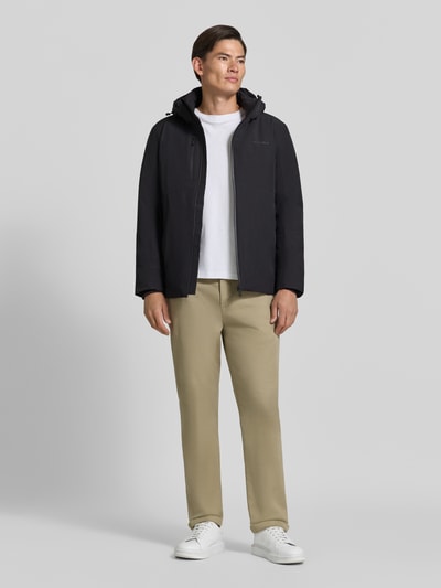 Męski model nosi Regular Fit Jacke mit Logo-Print von Lindbergh z elastycznej mieszanki materiałów, czarna, kaptur z tunelzugiem, napoleońska kieszeń, długość tyłu w rozmiarze M: 74 cm, szerokość ramion w rozmiarze M: 46 cm, szerokość klatki piersiowej w rozmiarze M: 42 cm, długość rękawów w rozmiarze M: 62 cm, widok całej sylwetki z przodu.