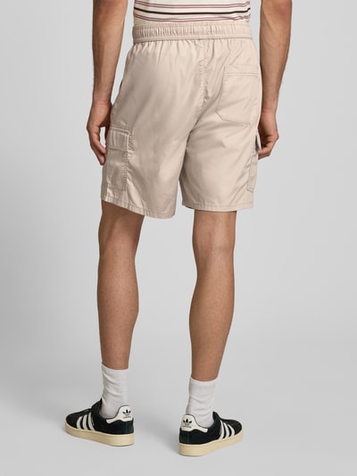Mężczyznamodel nosi Regular Fit Cargoshorts mit Baumwoll-Anteil von Only & Sons, beżowy materiał popelinowy, krój regular fit, elastyczny ściągacz w pasie, kieszeń z tyłu i cargo, jednolita faktura, widok całej sylwetki od tyłu.