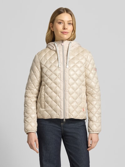 Frauenmodel trägt Regular Fit Jacke in Stepp-Optik Modell 'YOSIE' von Frieda & Freddies in Beige mit Kapuze, Reißverschluss, Eingrifftaschen, Logo-Applikation, elastische Ärmelabschlüsse, Ganzkörperansicht von vorne.