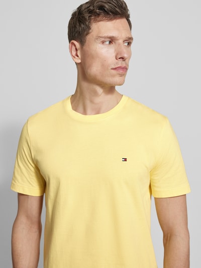 Mannenmodel draagt Regular Fit T-Shirt aus reiner Baumwolle van Tommy Hilfiger in effen geel, kortemouw, ronde hals, logo-stitching, materiaal jersey van katoen, close-up bovenlichaam voorkant.