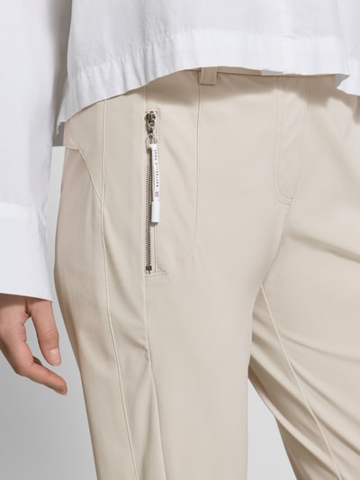 Kobiece model prezentuje Stoffhose in 7/8-Länge mit Stretch-Anteil Modell 'NATINA' od Raffaello Rossi, beżowy kolor, elastyczny materiał, dopasowany krój slim fit, elastyczny pasek z szlufkami, kieszenie na zamek, Szerokość w rozmiarze 36: 40 cm, Długość wewnętrzna nogawki: 69 cm, zbliżenie na górną część nogawki z przodu
