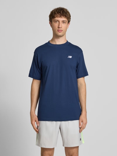 Männermodel trägt T-Shirt mit Logo und Rundhalsausschnitt von New Balance, Herren T-Shirt aus reiner Baumwolle, Regular-Fit, Dunkelblau, Logo-Print, Rückenlänge 74 cm bei Größe M, Ganzkörperansicht von vorne.