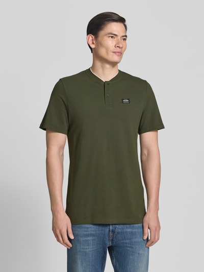 Männermodel trägt Regular Fit Poloshirt aus Baumwoll-Mix von s.Oliver RED LABEL in Olivgrün, unifarben, kurzarm, Ganzkörperansicht von vorne.