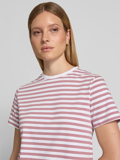 Kobiece model nosi damski t-shirt z mieszanki bawełny i elastanu, krój regular fit, model 'NORA' od VILA, okrągły dekolt, długość tyłu 57 cm w rozmiarze S, różowe i białe paski, tekstura gładka, zbliżenie na górną część ciała z przodu.