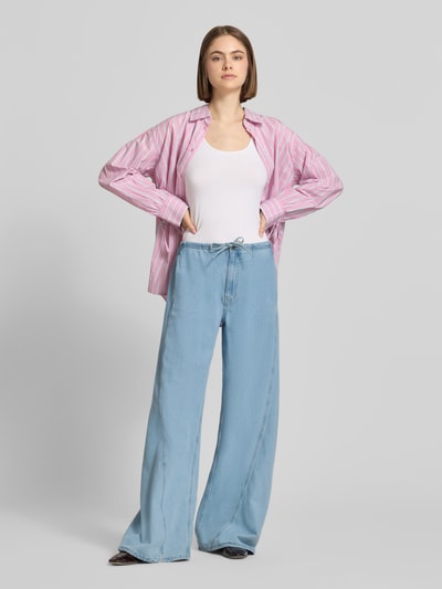 Frauenmodel trägt Low Rise Jogpants mit weitem Bein von Guess Jeans aus Baumwoll-Lyocell-Mix, Tunnelzug, hellblau, Ganzkörperansicht von vorne.