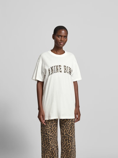 Frauenmodel trägt Oversized T-Shirt aus reiner Baumwolle von Anine Bing mit Rundhalsausschnitt, Label-Print und Halbarm, Ganzkörperansicht von vorne.