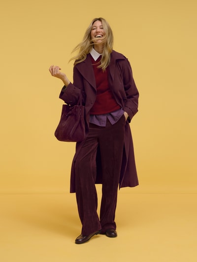 Frauenmodel trägt Regular Fit Trenchcoat aus Viskose-Mix von Jake*s Collection in dunklem Rotton vor gelbem Hintergrund, Ganzkörperansicht von vorne.