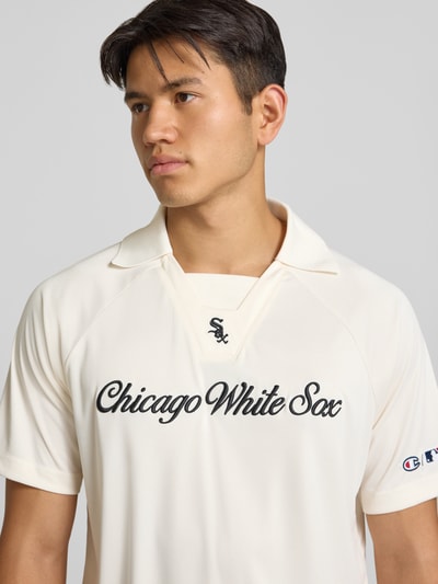 Männermodel trägt Relaxed Fit Poloshirt mit Logo-Stitching von Champion in Creme mit schwarzem Schriftzug, Nahaufnahme Oberkörper. Herren Poloshirt, Polokragen, kurzärmeliges Design, Rückenlänge bei Größe M: 70 cm.