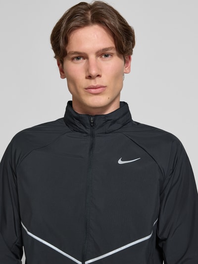 Männermodel trägt Regular Fit Jacke mit Stehkragen Modell 'Miler' von NIKE TRAINING, Schwarz mit Logo-Print, Nahaufnahme Oberkörper. Rückenlänge Größe M: 67 cm, Ärmellänge 64 cm, Reißverschluss.