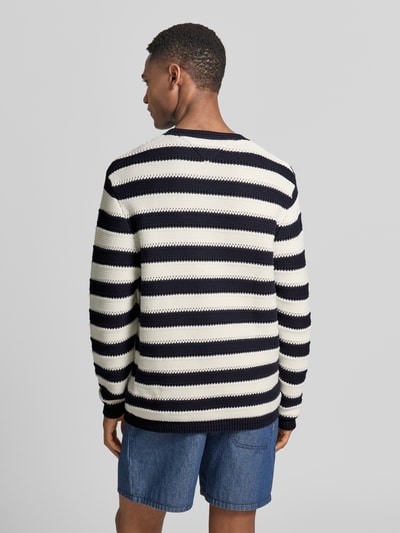 Männermodel trägt Regular Fit Strickpullover aus reiner Baumwolle von Tommy Hilfiger, Optik:Allover-Muster, gestreift, Ganzkörperansicht Rückansicht.