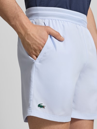 Mężczyzna nosi Loose Fit Sport-Shorts mit Mesh-Bund od Lacoste, jednokolorowy efekt, wyhaftowane logo, elastyczny pas, wpuszczane kieszenie, podłużna struktura materiału, siateczkowy pas; zbliżenie na biodra i udo z przodu.