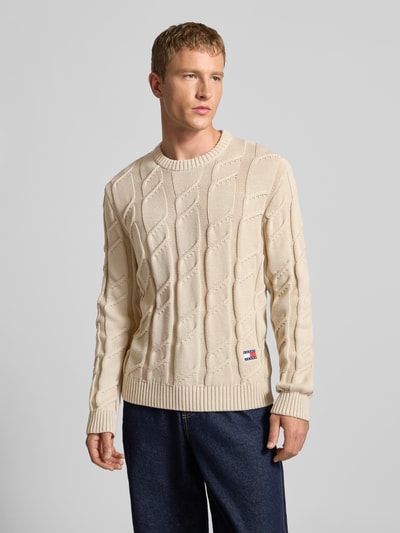 Männermodel trägt Regular Fit Strickpullover aus reiner Baumwolle von Tommy Jeans, Optik: Unifarben, Zopfmuster, Ganzkörperansicht von vorne.