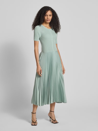 Vrouwenmodel draagt Regular Fit Businesskleid uit verschillende materialen model 'FADRIDI' van BOSS, effen kleuren, midilengte, ronde hals, plissérok van satijn, korte mouw, materiaalverwerking ribtricot, satijn, plissé, lichtgroen, gladde en geribde texturen, geheel te zien van voren.