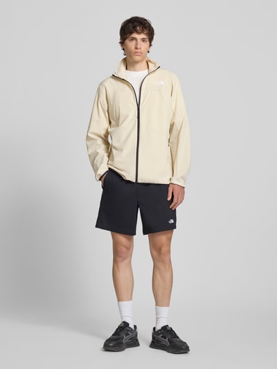 Männermodel trägt Regular Fit Jacke mit Stehkragen Modell 'Mountain' von The North Face in Beige, schwarzer Reißverschluss, Logo-Print, elastische Abschlüsse, Material-Mix, Ganzkörperansicht von vorne.