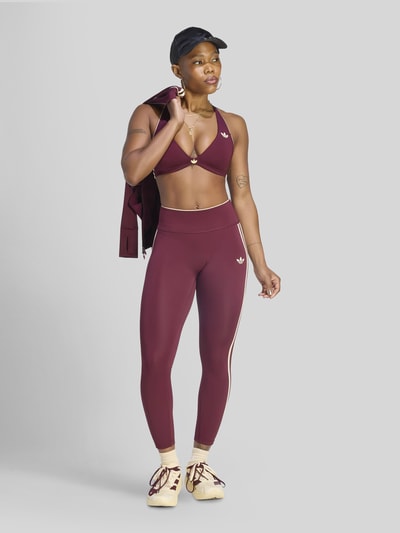 Frauenmodel trägt Slim Fit Sport-Leggings mit CLIMACOOL Technologie von adidas Training in dunklem Rot mit cremeweißen Streifen, Ganzkörperansicht von vorne.