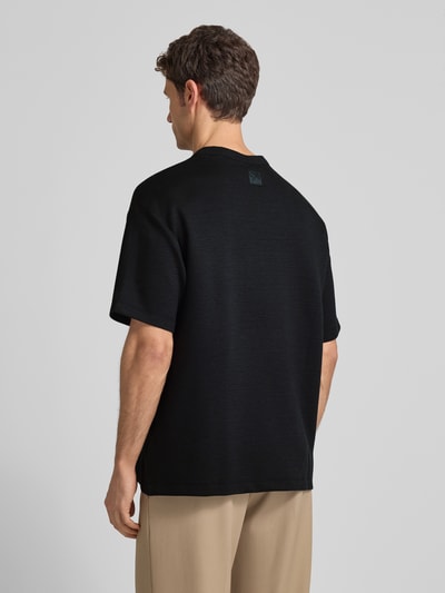 Männermodel trägt T-Shirt mit Rundhalsausschnitt Modell 'CRINKLE CREPE SPACER' von CK Calvin Klein, schwarzes Strukturmuster, Ganzkörperansicht Rückansicht.