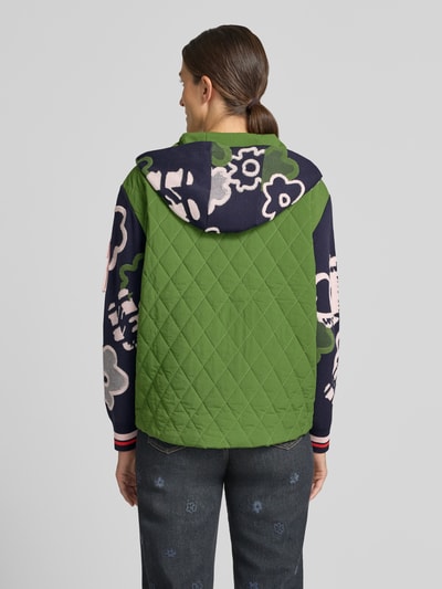 Frauenmodel trägt Regular Fit Jacke mit floralem Allover-Stitching von Marc Cain in Grün und Dunkelblau, gesteppt, Ganzkörperansicht Rückansicht.