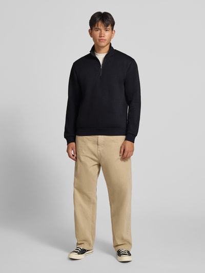 Männermodel trägt Regular Fit Sweatshirt mit Baumwoll-Anteil Modell 'Bradley' von JACK & JONES in Schwarz-Beige, Ganzkörperansicht von vorne, Herren Sweatshirt, Material-Mix, Troyer-Kragen, Rückenlänge 68 cm, Ärmellänge 66 cm.
