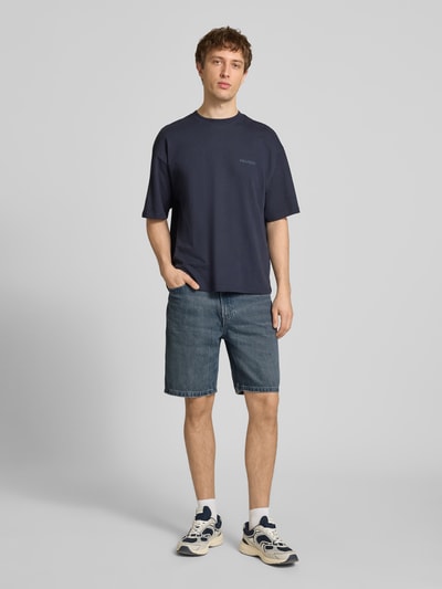 Męski model nosi Loose Fit Jeansshorts aus reiner Baumwolle von Calvin Klein Jeans, niebieski denim, 5 kieszeni, przód, całopostaciowe ujęcie.