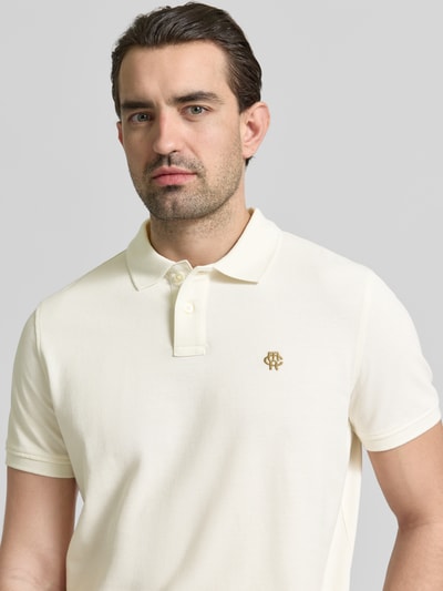 Männermodel trägt Slim Fit Poloshirt mit Logo-Stitching von MCNEAL in Creme, reine Baumwolle, Polokragen, Nahaufnahme Oberkörper.