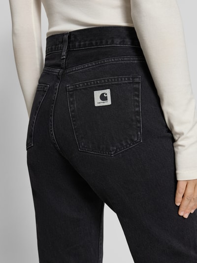 Kobieta modelka nosi jeansy z wpuszczanymi kieszeniami Jeans mit Eingrifftaschen Model 'Noxon' od Carhartt Work In Progress, bawełna, krój relaxed fit, kolor ciemny, detal tylnej kieszeni, widok z tyłu, długość wewnętrzna nogawki 79 cm, szerokość w pasie 36 cm, rozmiar 27, model damski, widok szczegółowy.