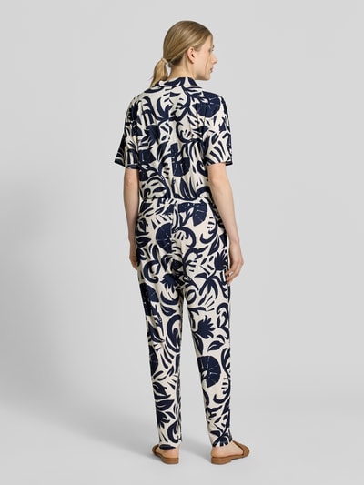 Vrouwenmodel draagt Jumpsuit met floralem allover-print van Oui in donkerblauw en crème, elastische materiaalmix, getailleerd, reverskraag, knoopsluiting, met korte mouwen, all-over bloemenprint, rechte pijpen, ruglengte maat 36: 146 cm, borstwijdte 51 cm, mouwlengte 13 cm, totale lengte 146 cm, binnenbeenlengte 76 cm. Ganzkörperansicht rückansicht.
