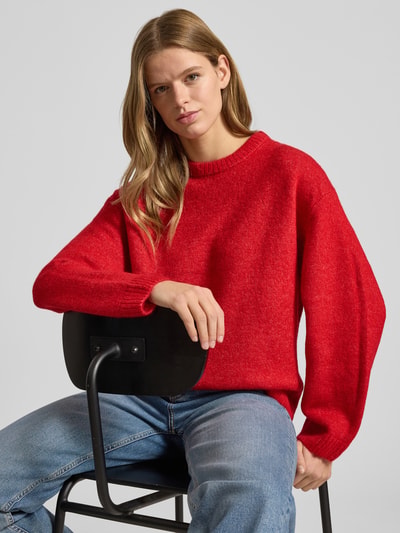 Vrouwenmodel draagt Strickpullover mit Woll-Anteil van Gina Tricot, rood, geribde boorden, ronde hals, detailopname bovenlichaam.