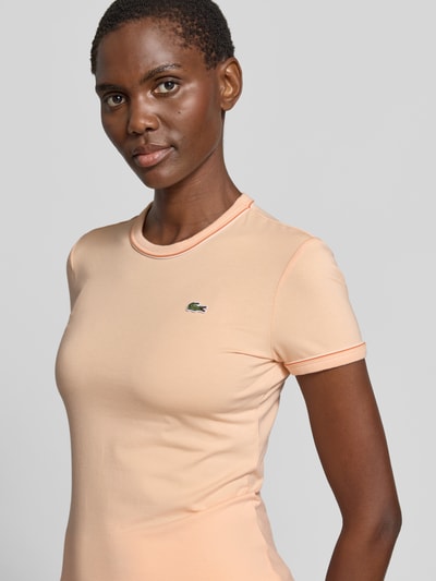Frauenmodel trägt Slim Fit T-Shirt aus Baumwoll-Mix von Lacoste in Apricot mit Logo-Stitching und Kontrastpaspel, Nahaufnahme Oberkörper.