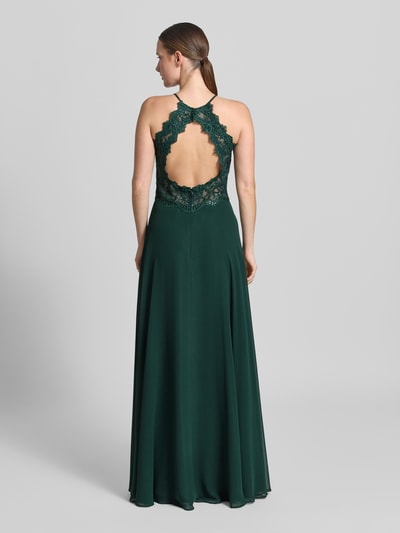 Frauenmodel trägt Abendkleid mit floralem Spitzenbesatz von Vera Mont in Dunkelgrün, Maxilänge, ärmellos, Rückseitiger Cut Out, Ganzkörperansicht Rückansicht.