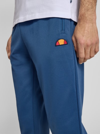 Męski model nosi spodnie dresowe z mieszanki bawełny Ellesse Sweatpants mit elastischem Bund Modell 'BERTONI', krój regular fit, detal z logo, długość wewnętrzna nogawki w rozmiarze M: 76 cm, niebieski, zbliżenie na górną część nogawki.