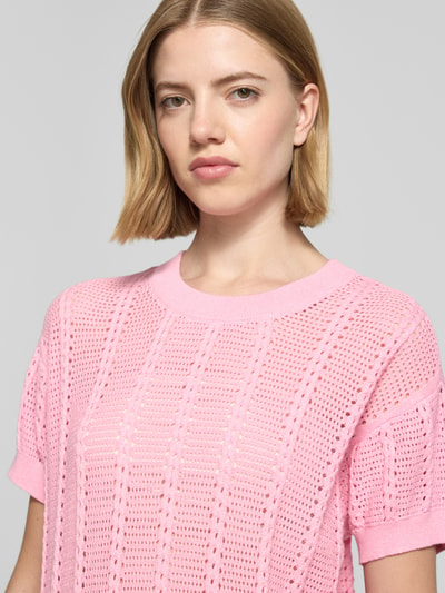 Modelka kobieca nosi Relaxed Fit Strick-Shirt aus Baumwoll-Mix Modell 'LUX LIGHT' od Vero Moda, różowy, jednolity, dziurkowany wzór, krótki rękaw, wykończenie ściągaczem, dekolt okrągły, materiał bawełniany, ujęcie: zbliżenie górnej części ciała.