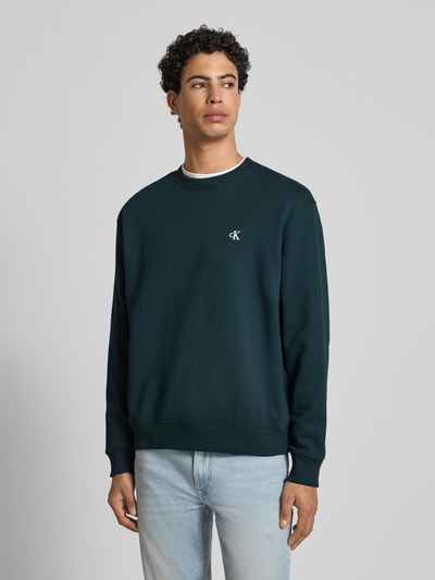 Männermodel trägt Sweatshirt aus reiner Baumwolle von Calvin Klein Jeans in Dunkelgrün mit Rundhalsausschnitt, Label-Stitching, gerader Schnitt, gerippte Abschlüsse, Rückenlänge 65 cm, Ärmellänge 63 cm, Ganzkörperansicht von vorne.