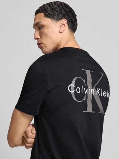 Männermodel trägt Regular Fit T-Shirt mit Logo-Print von Calvin Klein Jeans in Schwarz, reine Baumwolle, Nahaufnahme Oberkörper.