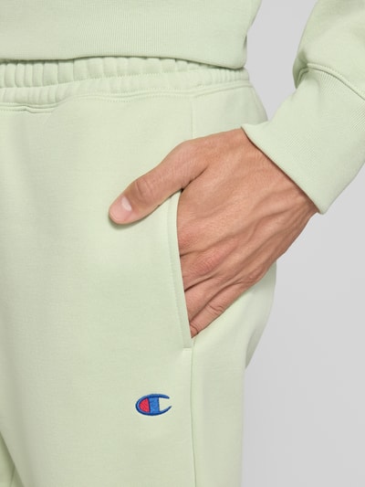 Männermodel trägt Sweatpants mit Label-Detail von Champion in Hellgrün, Baumwollmischung, Nahaufnahme Hüfte und Hand, Detailaufnahme.