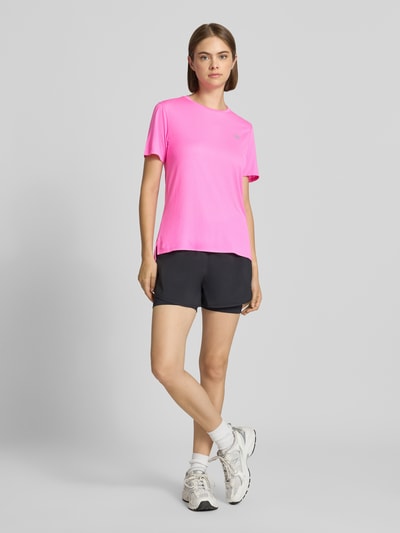 Frauenmodel trägt Regular Fit T-Shirt mit Logo-Print von New Balance in Pink, Kurzarm, verlängerte Rückseite, Ganzkörperansicht von vorne.