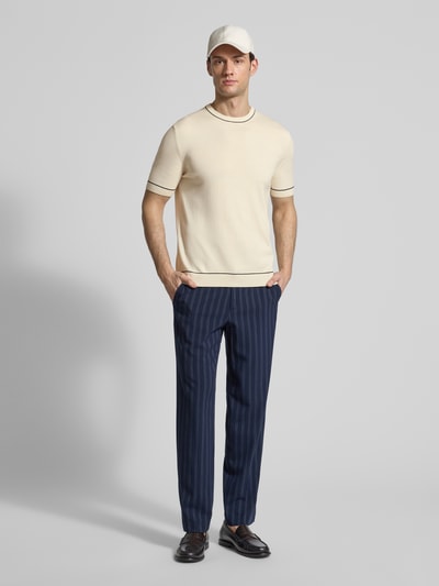 Männermodel trägt Strickshirt mit Rundhalsausschnitt von Gant in Beige aus Baumwoll-Modal-Mix, kurze Ärmel, gerade Form, Ganzkörperansicht von vorne.
