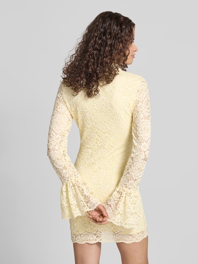 Frauenmodel trägt Slim Fit Minikleid mit Allover-Spitzenbesatz von Gina Tricot in zartem Gelb, langärmelig, Rückenansicht, Ganzkörperansicht Rückansicht. Elastischer Material-Mix, Stehkragen, Schlüsselloch-Ausschnitt, Rückenlänge 85 cm, Brustweite 38 cm, Ärmellänge 68 cm, strukturierte Spitzen-Textur.