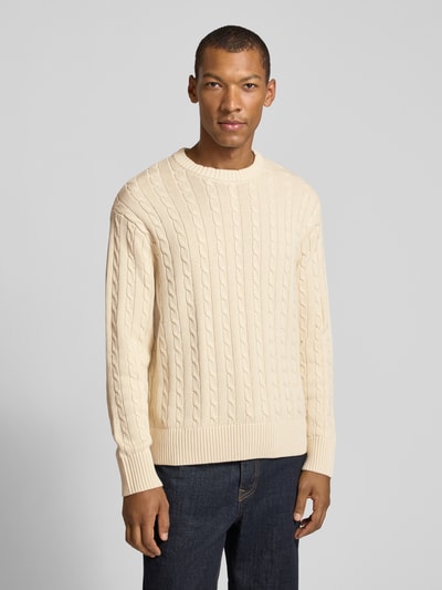 Männermodel trägt Relaxed Fit Pullover aus reiner Baumwolle Modell 'BRAUN' von Selected in creme mit Zopfmuster, Strickoptik, Ganzkörperansicht von vorne.