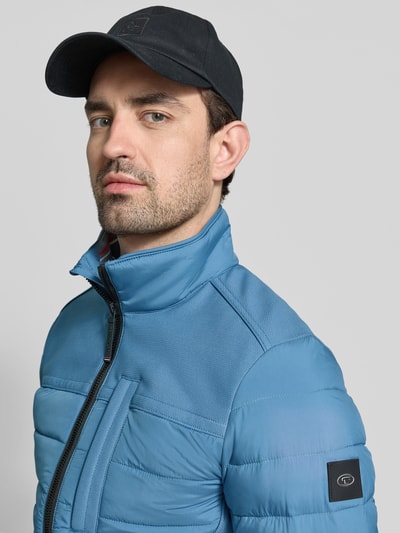 Männermodel trägt Regular Fit Steppjacke mit seitlichen Stretcheinsätzen von Tom Tailor, niebieski, jednolity kolor, zamek, stójka, logo, elastyczne wykończenia, detal na plecach, kieszeń na piersi, hydorfobowy materiał, krój regular fit, zbliżenie na górną część ciała