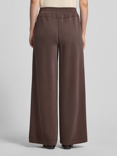 Vrouwenmodel draagt Wide Fit broek met viscose van comma in bruin, elastische band, sierstrik, materaailmix, wide fit, binnenbeenlengte 77 cm, bandwijdte 37 cm, maat 36. Volledige lichaamsaanzicht achteraan.