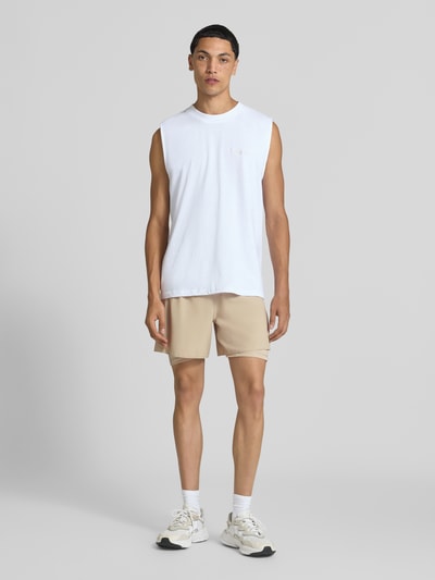 Männermodel trägt beigen Regular Fit Sportshorts mit Logo-Print Modell 'ADI365/// 2i1 M' von adidas, adidas Training, Ganzkörperansicht von vorne.