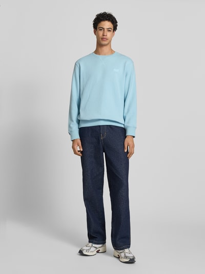Männermodel trägt Sweatshirt mit Rundhalsausschnitt und Label-Stitching von Superdry in Hellblau, Baumwoll-Mix, Regular-Fit, Ganzkörperansicht von vorne.